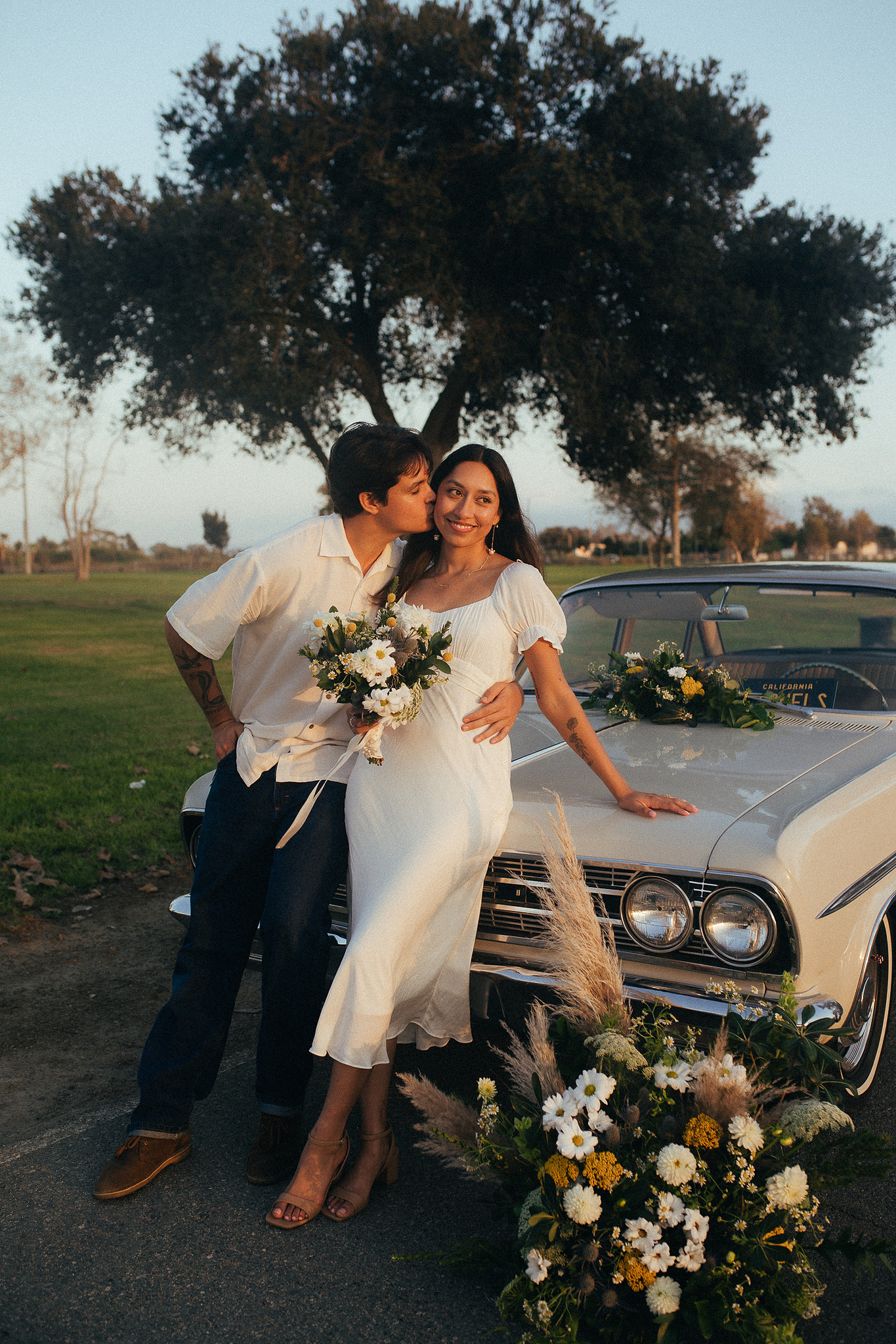 Two young lovebirds pose in front of their vintage car for their engagement photo session in Fairview Park, Costa Mesa, CA. Vibes are film and romantic. Engagement photography by Aly Rose Photo. California wedding photographer