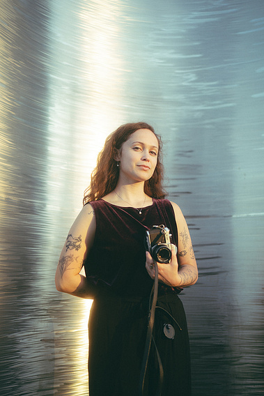 Portrait of the photographer, Aly Rose Photo. She stands, holding her film camera, in front of a luminescent art installation at Huntington Central Park, Huntington Beach, CA. Southern California film and digital Wedding Photographer