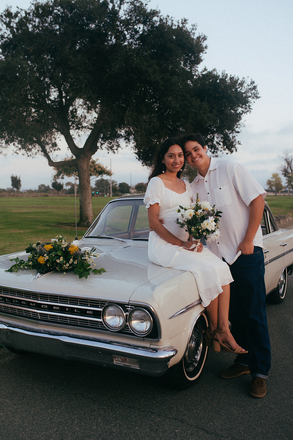 Two young lovebirds pose in front of their vintage car for their engagement photo session in Fairview Park, Costa Mesa, CA. Vibes are film and romantic. Engagement photography by Aly Rose Photo. California wedding photographer
