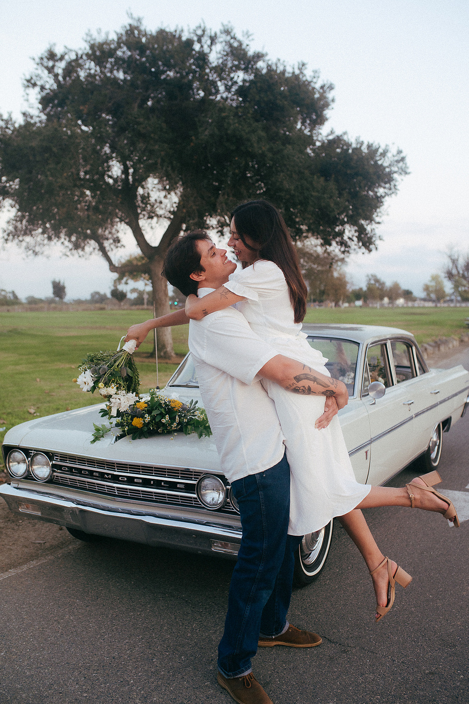 Two young lovebirds pose in front of their vintage car for their engagement photo session in Fairview Park, Costa Mesa, CA. Vibes are film and romantic. Engagement photography by Aly Rose Photo. California wedding photographer