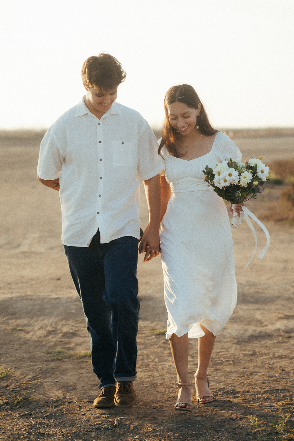 Two young lovebirds walk through chaparral hills during golden hour for their engagement photo session in Fairview Park, Costa Mesa, CA. Natural light engagement photography by Aly Rose Photo. California wedding photographer