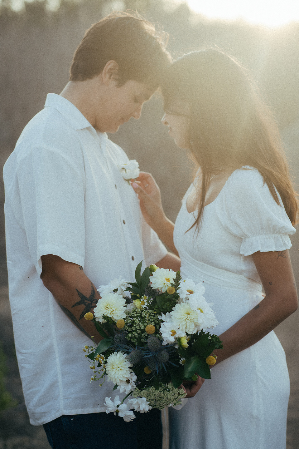 Two young lovebirds pose in a cottage-core white dress and dress shirt at golden hour for their engagement photo session in Fairview Park, Costa Mesa, CA. Natural light engagement photography by Aly Rose Photo. California wedding photographer