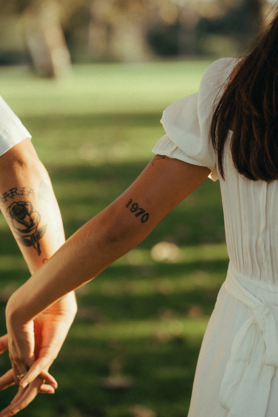 Two young lovebirds hold hands and stroll through the grass in the afternoon sun for their engagement photo session in Fairview Park, Costa Mesa, CA. Engagement photography by Aly Rose Photo. California wedding photographer
