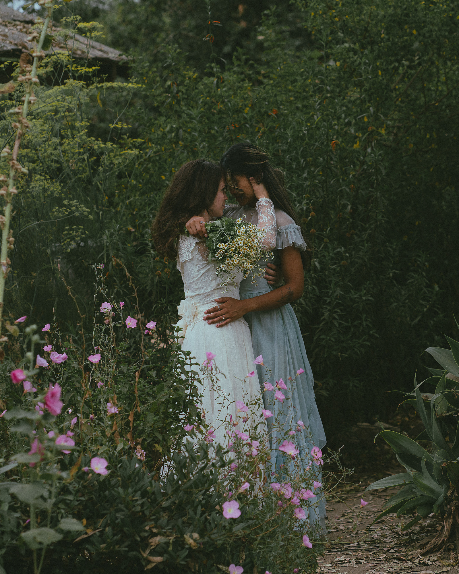 Romantic, cottagecore, fairytale, LGBTQ portrait session in San Juan Capistrano, Orange County, CA. A woman in a blue dress kisses the hand of a woman in a white dress holding wildflowers. Photography by Aly Rose Photo, CA wedding, elopement photographer