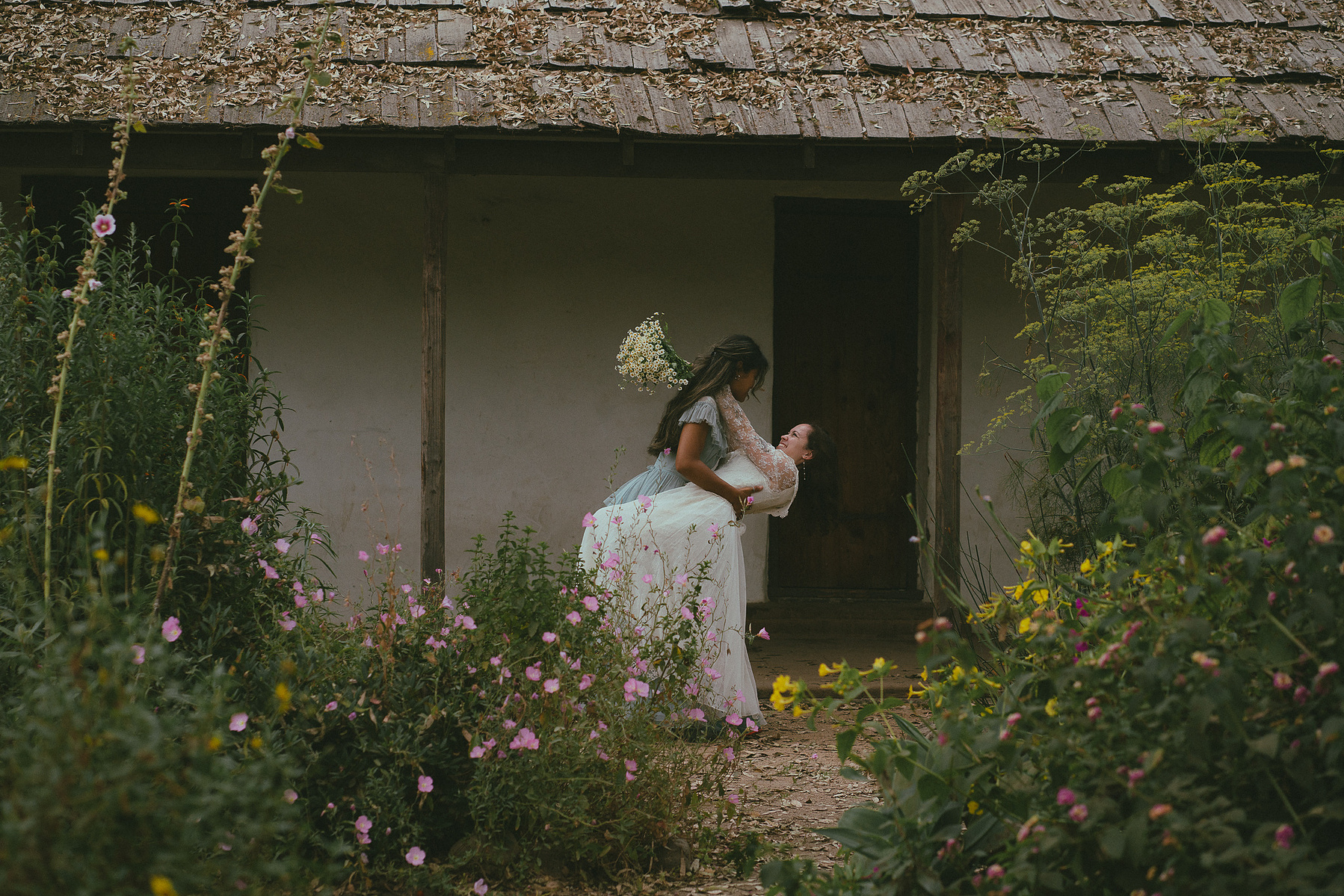 Romantic, cottagecore, fairytale, LGBTQ portrait session in San Juan Capistrano, Orange County, CA. A woman in a blue dress kisses the hand of a woman in a white dress holding wildflowers. Photography by Aly Rose Photo, CA wedding, elopement photographer