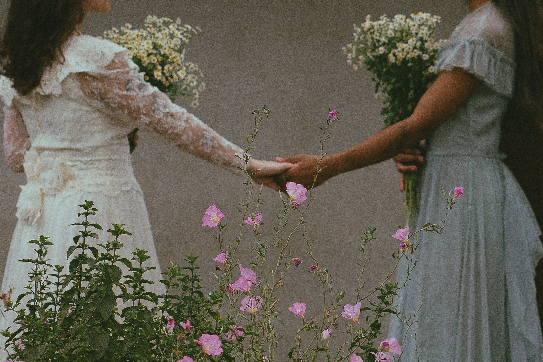 Romantic, cottagecore, fairytale, LGBTQ portrait session in San Juan Capistrano, Orange County, CA. A woman in a blue dress kisses the hand of a woman in a white dress holding wildflowers. Photography by Aly Rose Photo, CA wedding, elopement photographer
