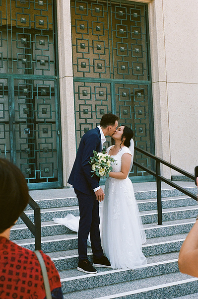 Bride and groom share their first kiss on the steps of the Los Angeles California Temple, church of LDS, after their temple sealing ceremony. Shot on 35mm film. Vibes are romantic, organic, dreamy. SoCal Wedding elopement photographer Aly Rose Photo.