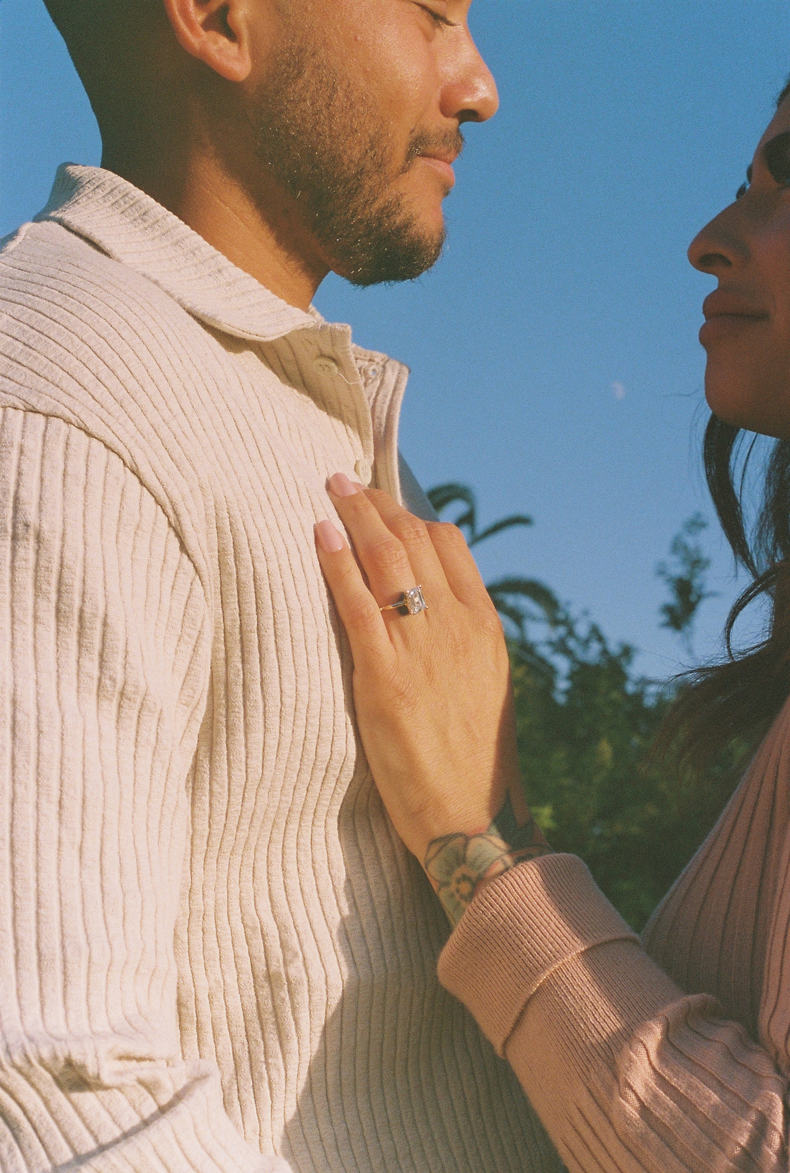 A 35mm film portrait of newly engaged fiances staring lovingly into each others eyes, ring, blue sky, and moon in shot. Relaxing sunset engagement photography in Fullerton, Southern CA by documentary wedding, elopement photographer Aly Rose Photo