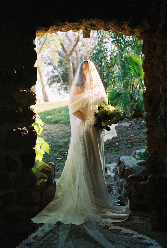 A dreamy, 35mm film portrait of the bride. She stands under a fairytale arch with the light hitting her veil, a green paradise surrounding her. Wedding photography by Aly Rose Photo, Southern California film and digital photographer