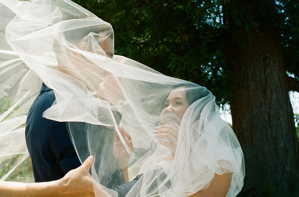 At their temple sealing, bride and groom get stuck under the veil for a dreamy, romantic shot at the Mormon Los Angeles California Temple LDS. 35mm film photo. Dreamy, romantic, cinematic, editorial. SoCal wedding elopement photographer Aly Rose