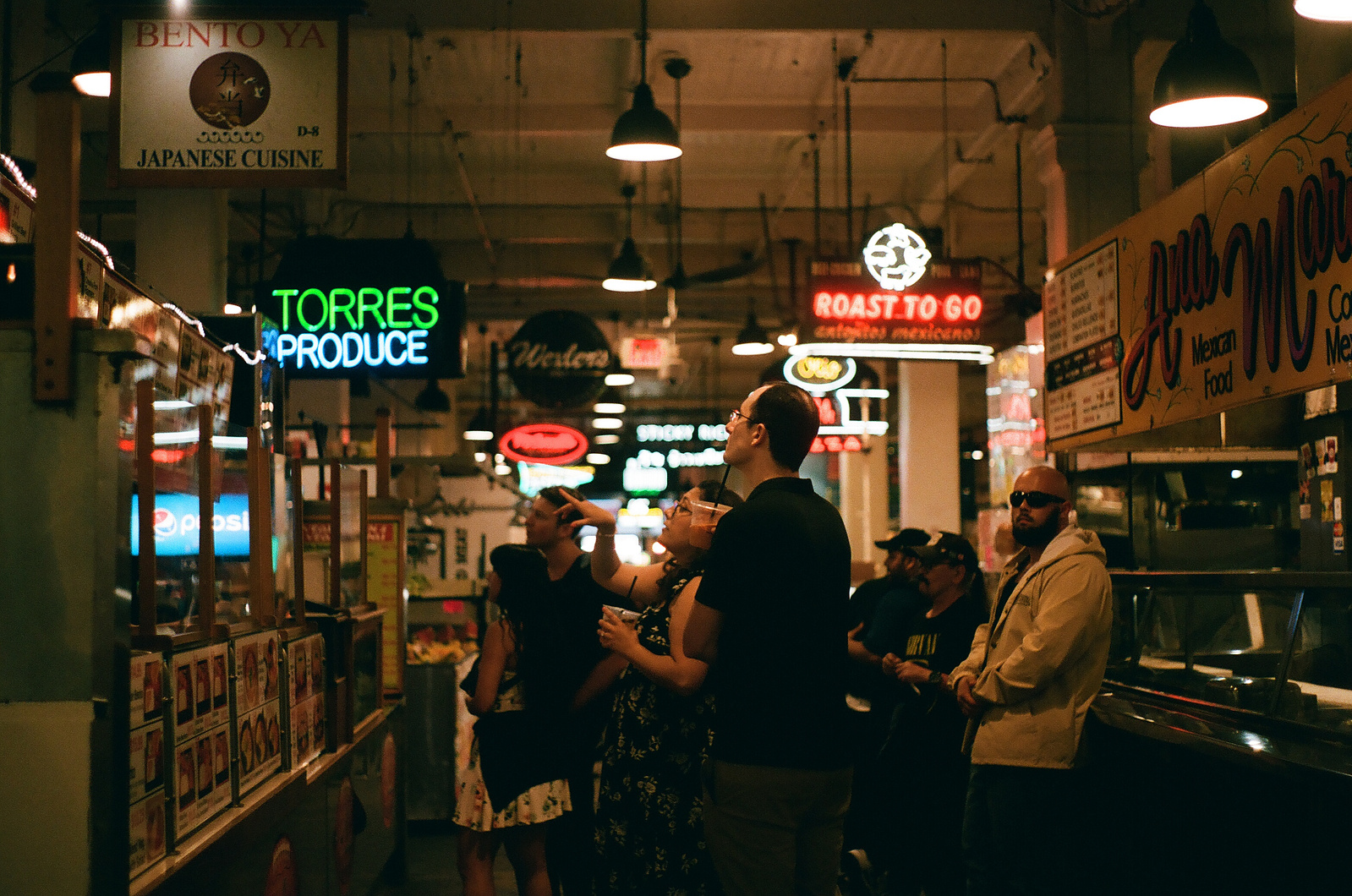 City life engagement shoot in downtown Los Angeles, CA. Engaged couple decide what dinner to order at the Grand Central Market in LA. 35mm film. Vibes are cinematic, romantic, organic, authentic. SoCal Wedding and elopement photographer Aly Rose Photo