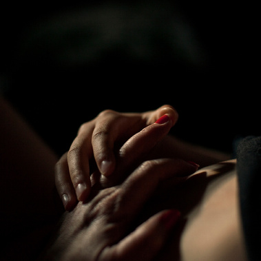 Two hands, mother and daughter, 
 intertwined surrounded by darkness, one red fingernail is prominent in the centre of the frame.