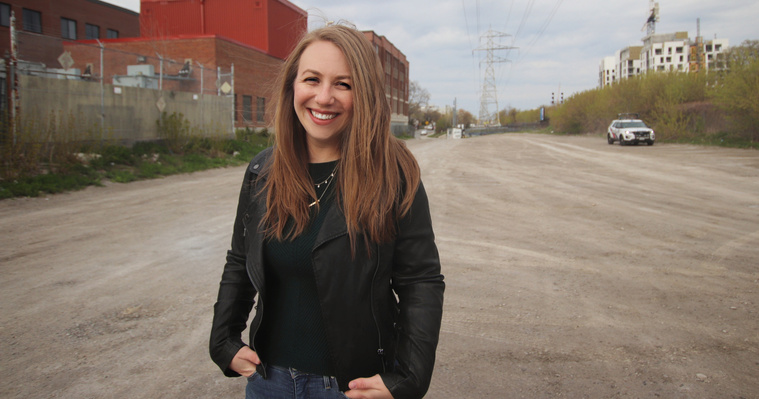 Martha Chomyn is smiling at the camera and wearing a leather jacket in a nearly deserted parking lot. 