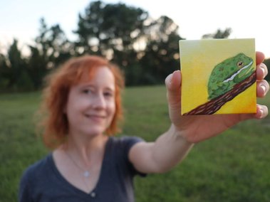Alex smiling and holding a small painting of a Barking Tree Frog