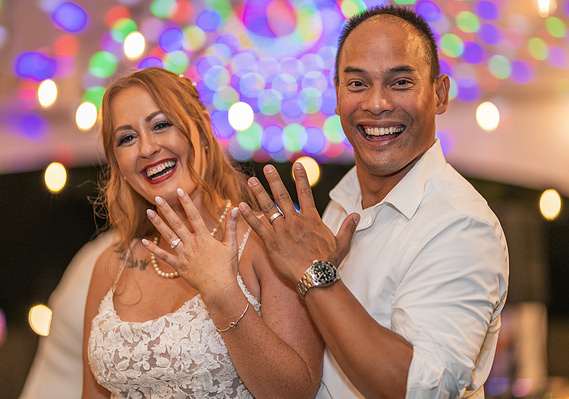 Wedding Photographer-Uniquely Created Photography. Bride and groom after the wedding with bright lights behind them. Showing off wedding rings.