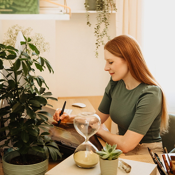 Eine Buchillustratorin sitzt beim Personal Branding Fotoshooting für ungestellte Businessfotos an ihrem Arbeitsplatz und zeichnet.