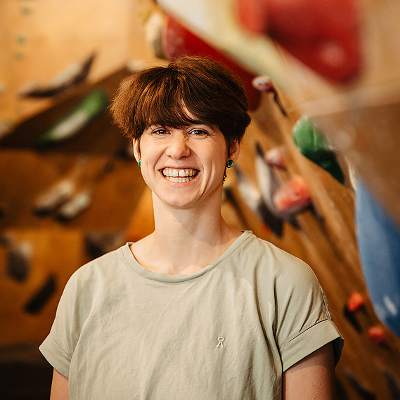 Die Klettertherapeutin blickt beim Fotoshooting in einer Boulderhalle mit einem natürlichen Lachen in die Kamera der Businessfotografin aus Berlin.