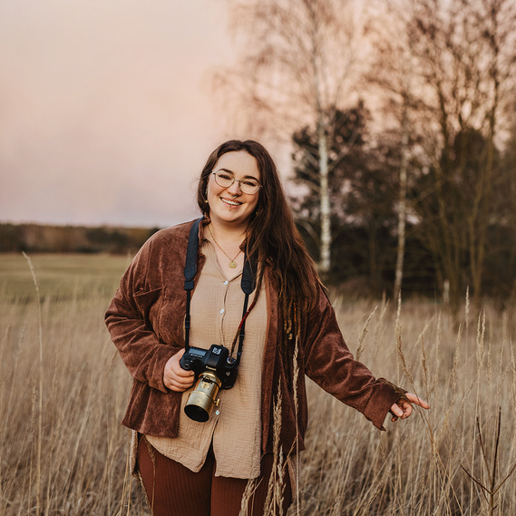 Die Businessfotografin Stefanie aus Berlin läuft beim Fotoshooting mit der Kamera in der Hand durch hohes Gras.

