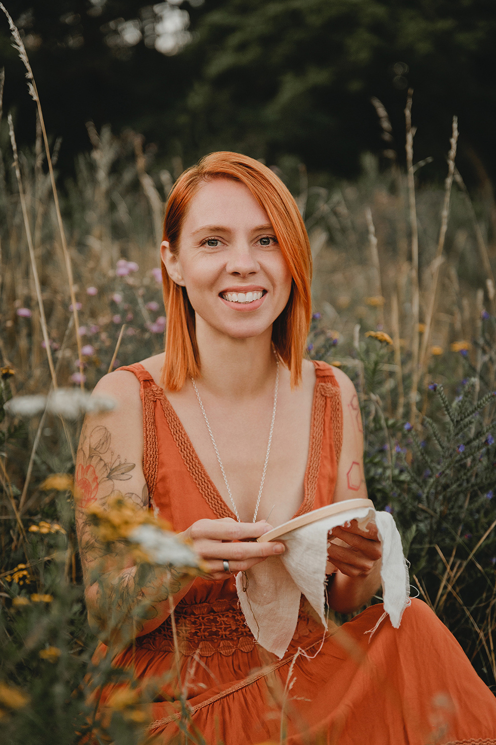 Eine Designerin sitzt bei einem Business Fotoshooting in der Natur zwischen Wildblumen und hält einen Stickrahmen in der Hand.
