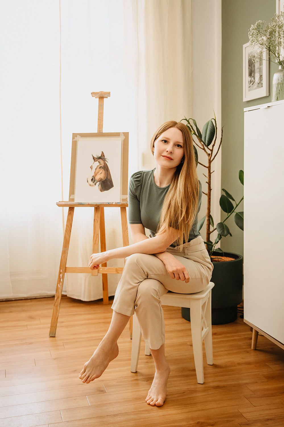 Eine Künstlerin sitzt beim Business-Fotoshooting in ihrem Atelier in Potsdam vor einer Staffelei auf einem Hocker.