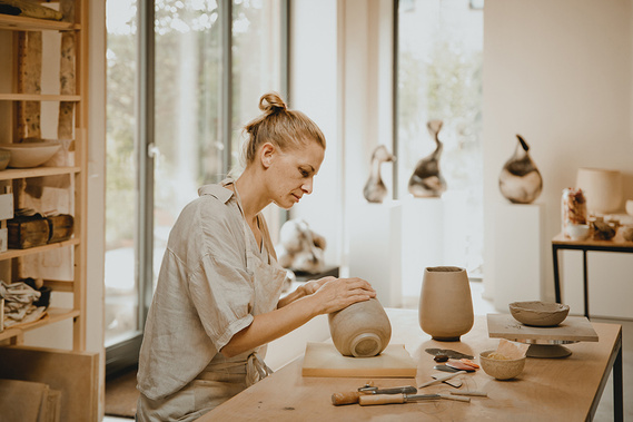 Eine Keramikerin aus Brandenburg sitzt in ihrem Atelier und töpfert eine Vase, während Businessfotos für ihre Webseite gemacht werden.