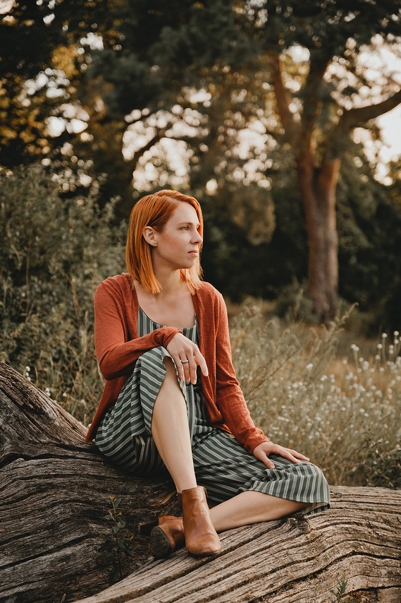 Bei einem entspannten Business Fotoshooting in der Natur sitzt eine Unternehmerin in lockerer Pose auf einem Baumstamm. 