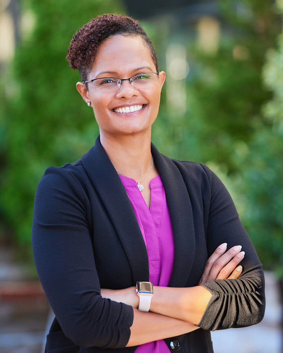 African-American woman with glasses, smiling with crossed, arms, professional headshot. With green backdrop.