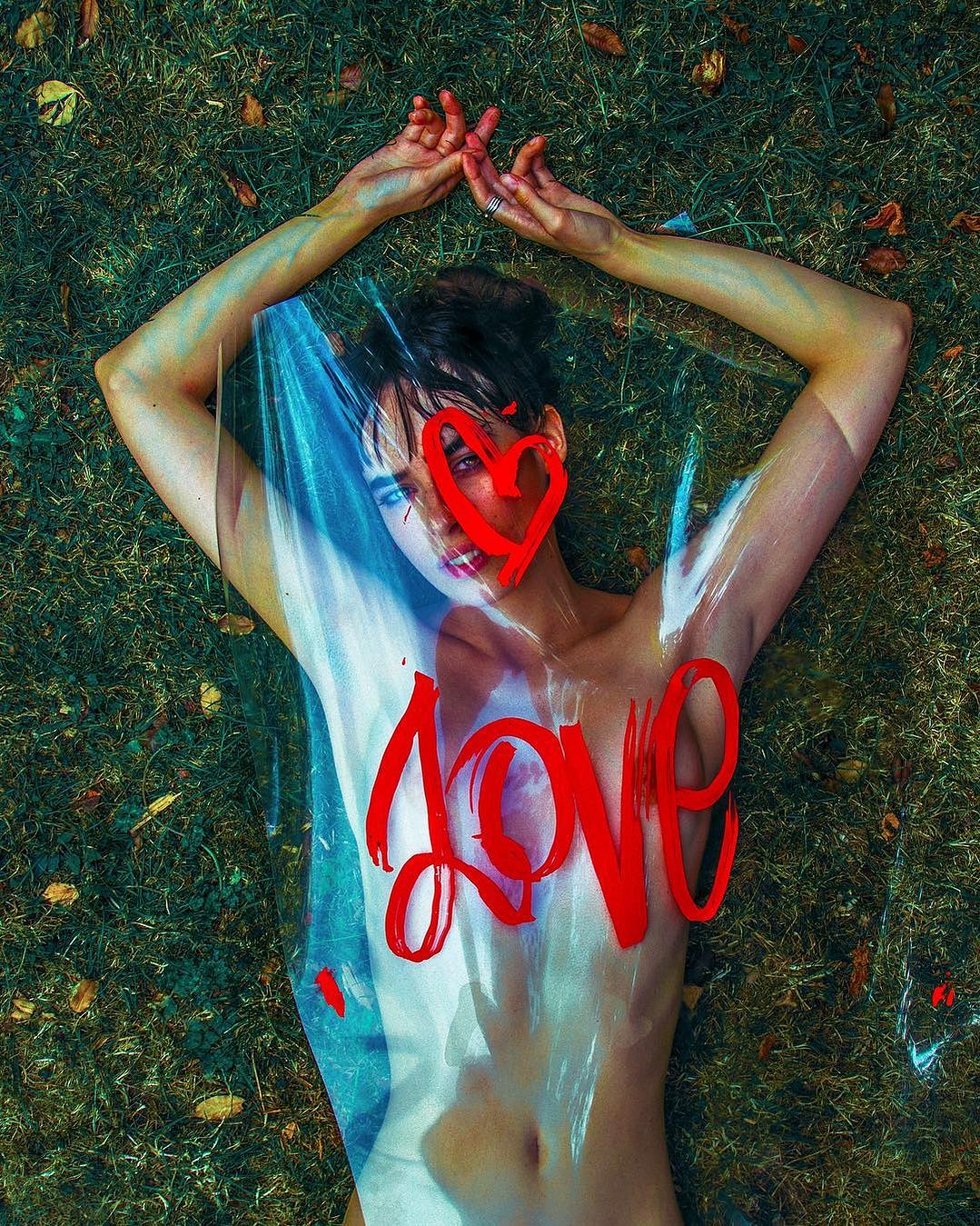 A woman lies on the ground beneath a cellophane sheet with the word "Love."