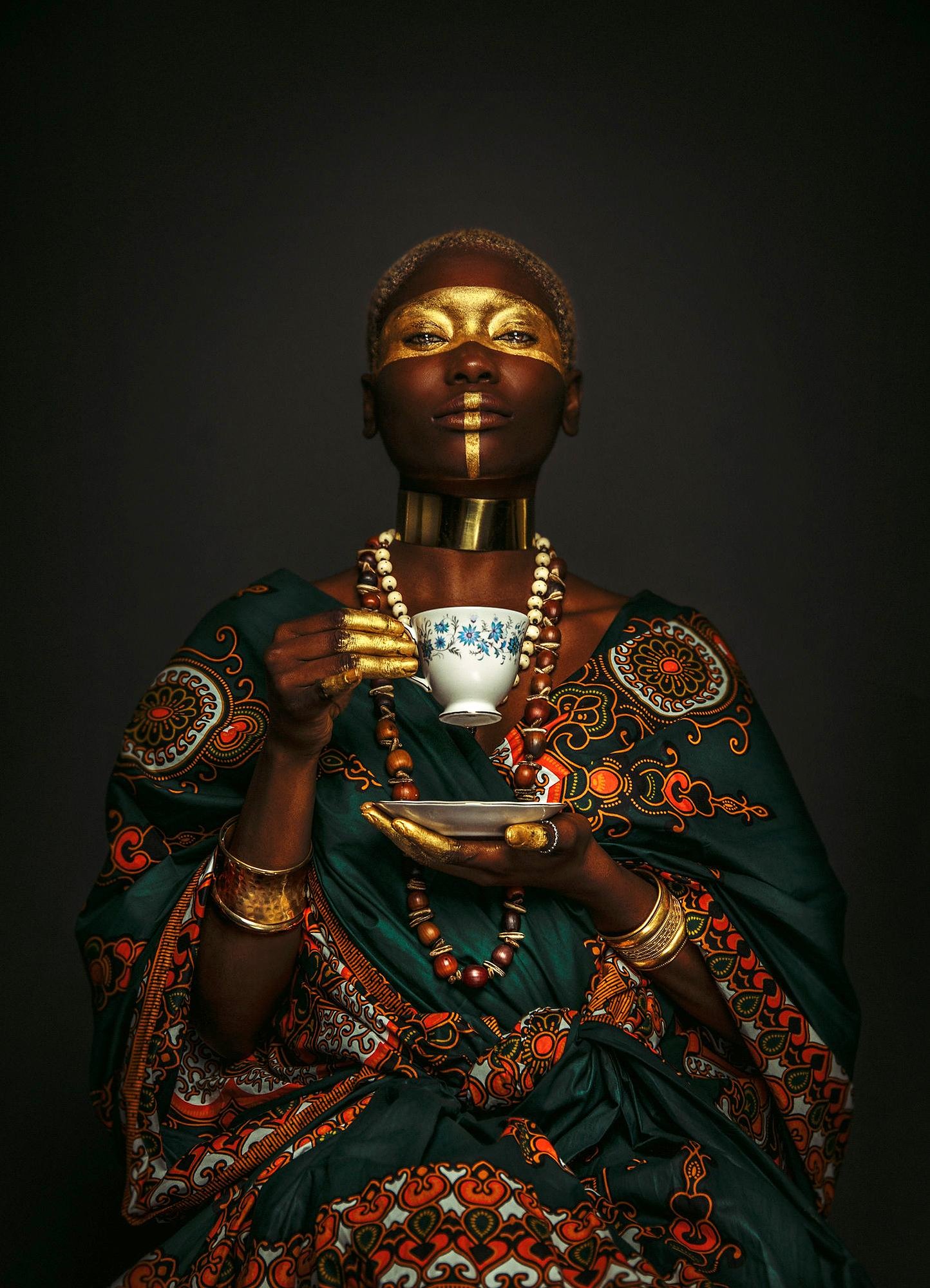 A woman sits in traditional West African garb, having tea from a white and blue porcelain cup.