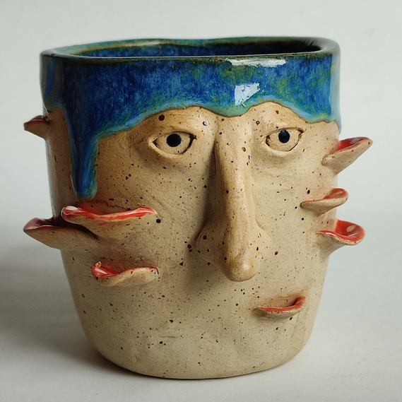 One handmade blue ceramic mug with eyes and a nose and mushrooms.