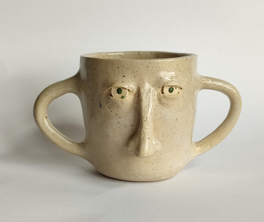 One handmade ceramic mug with eyes, a nose and two handles.
