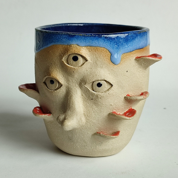 one handmade ceramic mug with eyes, a nose and mushrooms around.