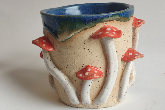 One handmade ceramic mug with mushrooms around.