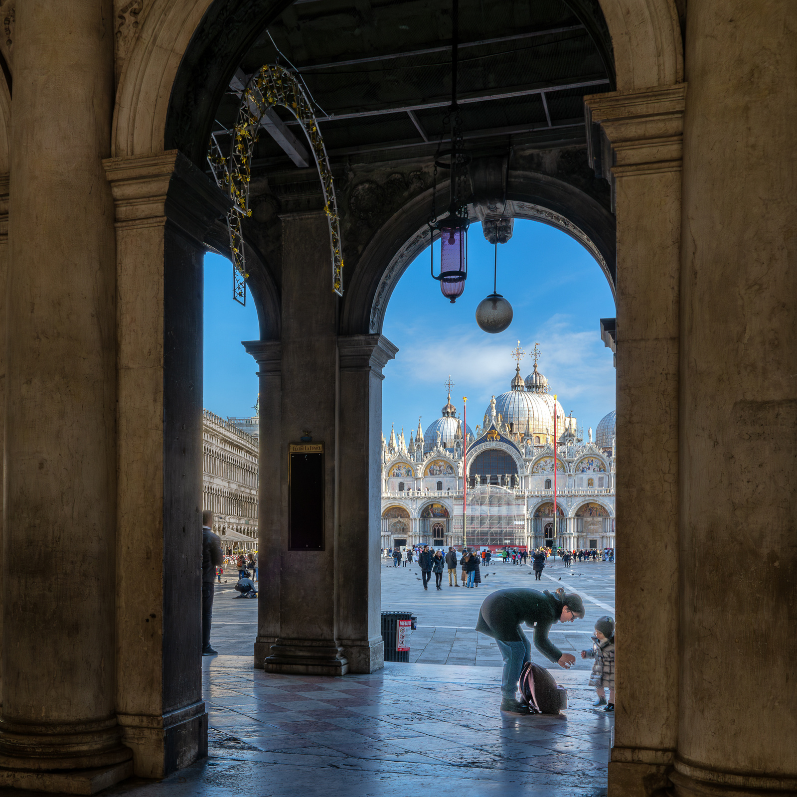 Cropped view of Mother with little girl framed in an archway with San Marco cathedral basilica of Venice Italy in background