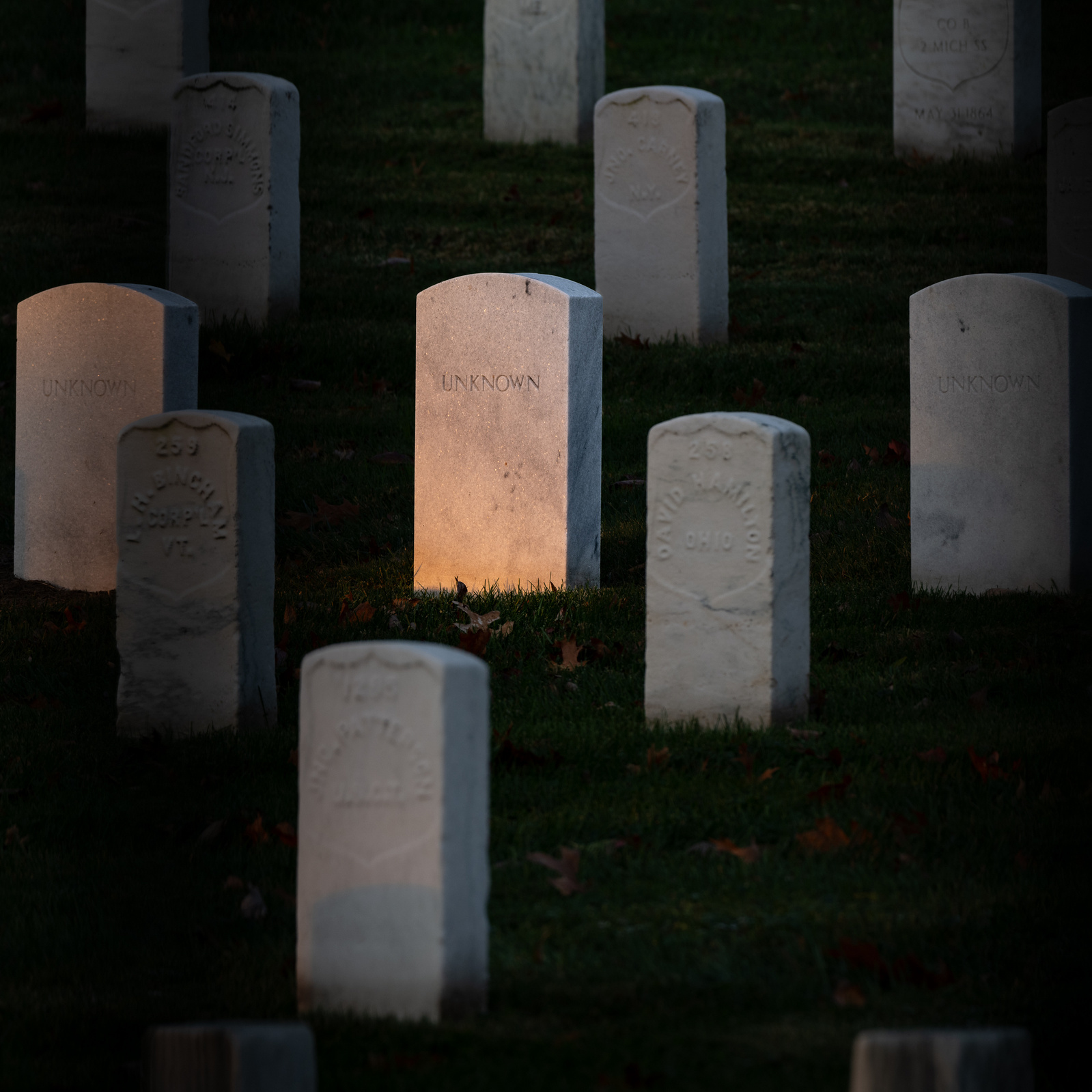 group of tombstones on a hillside at Arlington National Cemetery with one tombstone, engraved with the single word "unknown," lit by early morning sun