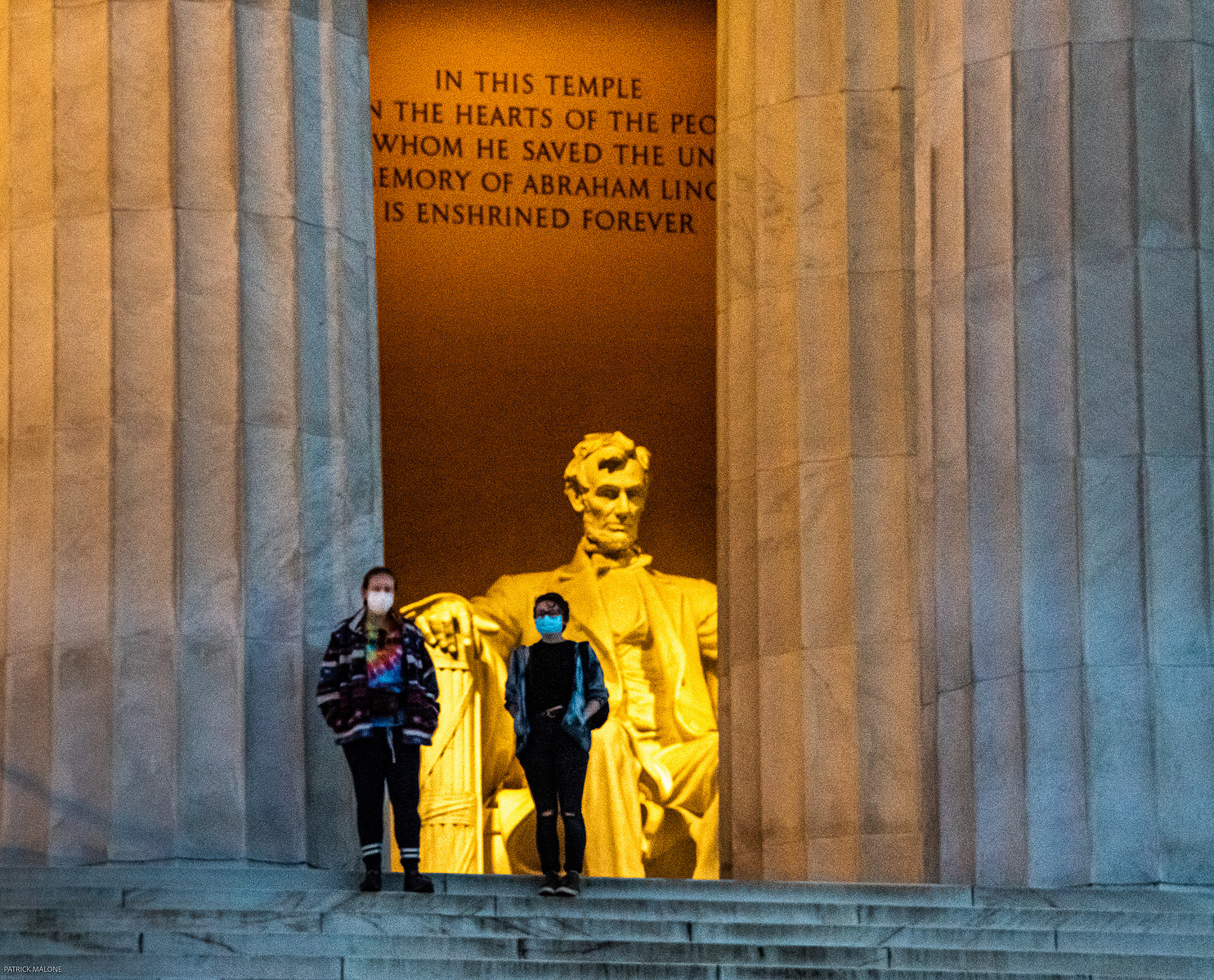 Two people framed by pillars looking out from the Lincoln Memorial, with Lincoln's statue behind them