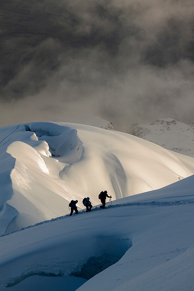 three people navigate a glacier. 