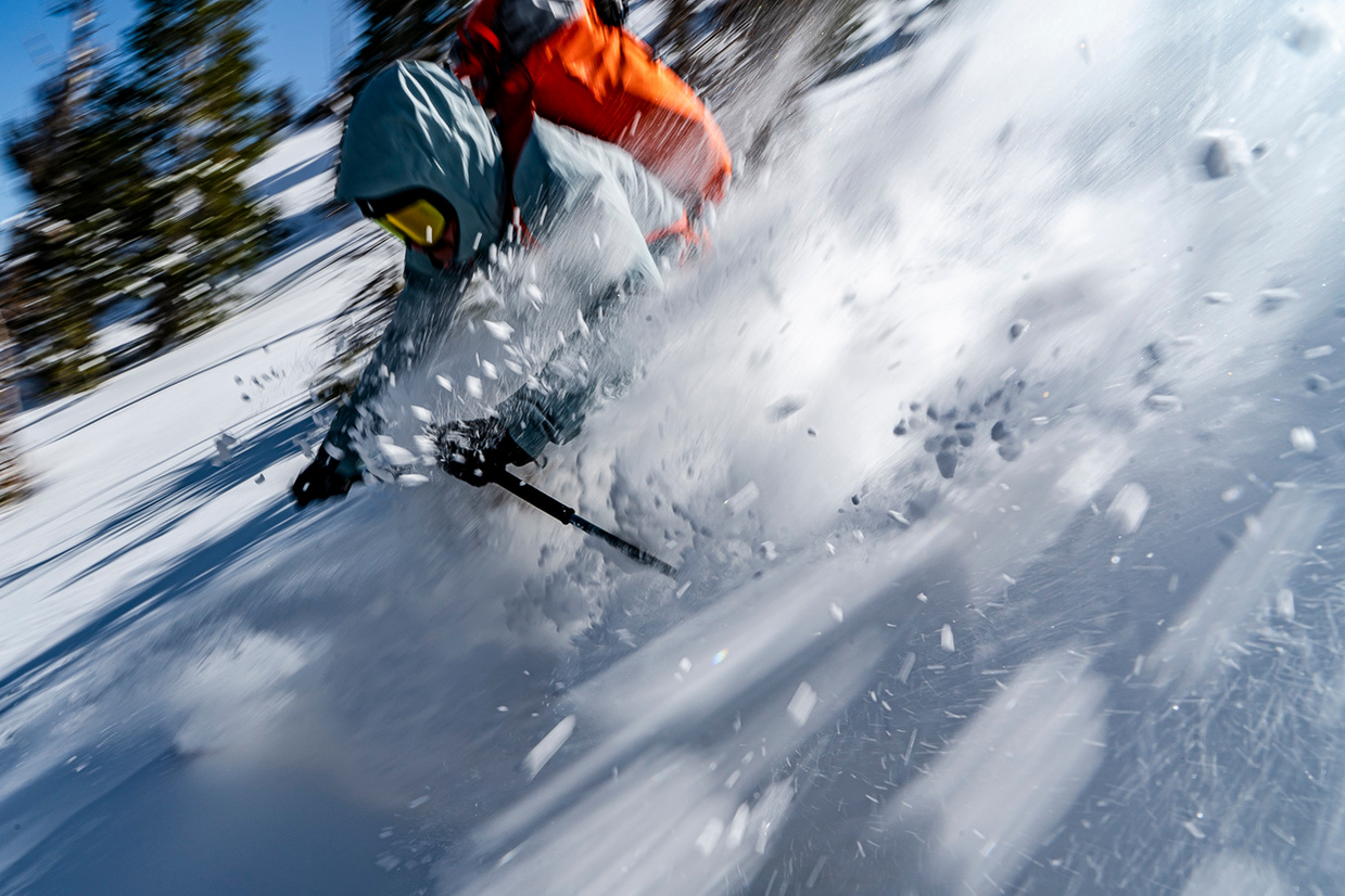 A skier skiing so fast the camera shows a motion blure as the skier goes by the photographer with snow going everywhere. 