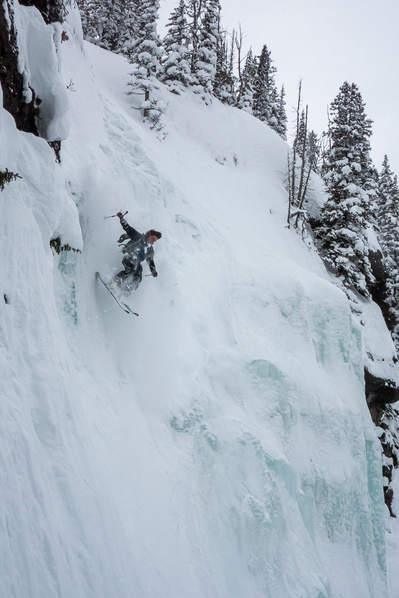 A skier skiing over a frozen waterfall on a very steep slope.