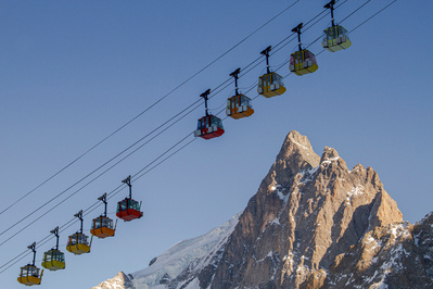 cable cars in la grave france beinging skiers from the valleys to teh galciers in the background a jagged steep granite rock mountain stands tall in the background with blue skies.
