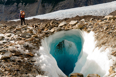 A women walks over an ice bridge. With rocks scattered on the glacier this ice bridge was formed as the glaciers continue to melt. The rocks absorb heat from the sun causing even faster melting rates. Authentic, adveture climate stock photography.