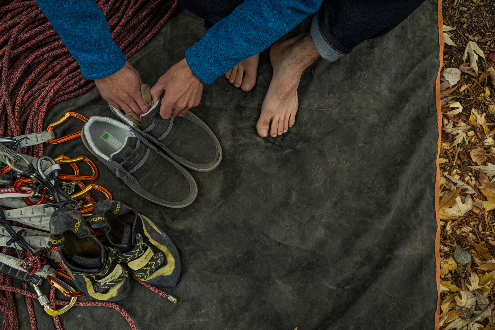 A young man is rock climbing with his street shoes and trransitioning into rock climbing attire.