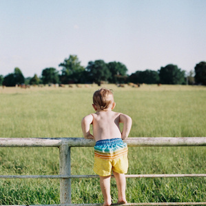 Boy stands on fence railing in swimsuit