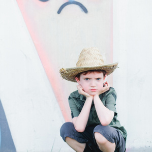 Boy in a cowboy hat sits next to grumpy wall mural