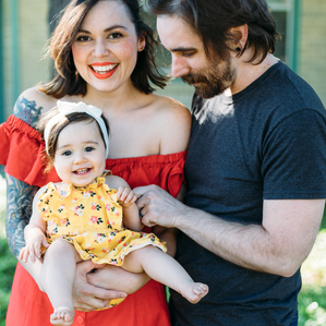 Mother and Father stand with baby girl in front yard