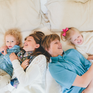 Older brother and sister laugh and tickle younger twin siblings on bed