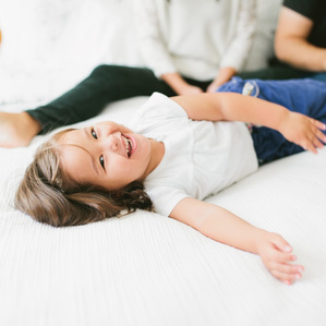 Little girl lays on bed laughing next to parents
