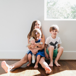 Kids sit together on skateboard in sunny dining room