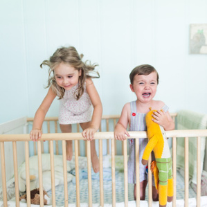 Brother cries while Sister laughs and jumps in crib