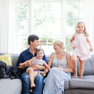 Couple smiles at each other on couch with kids and dog